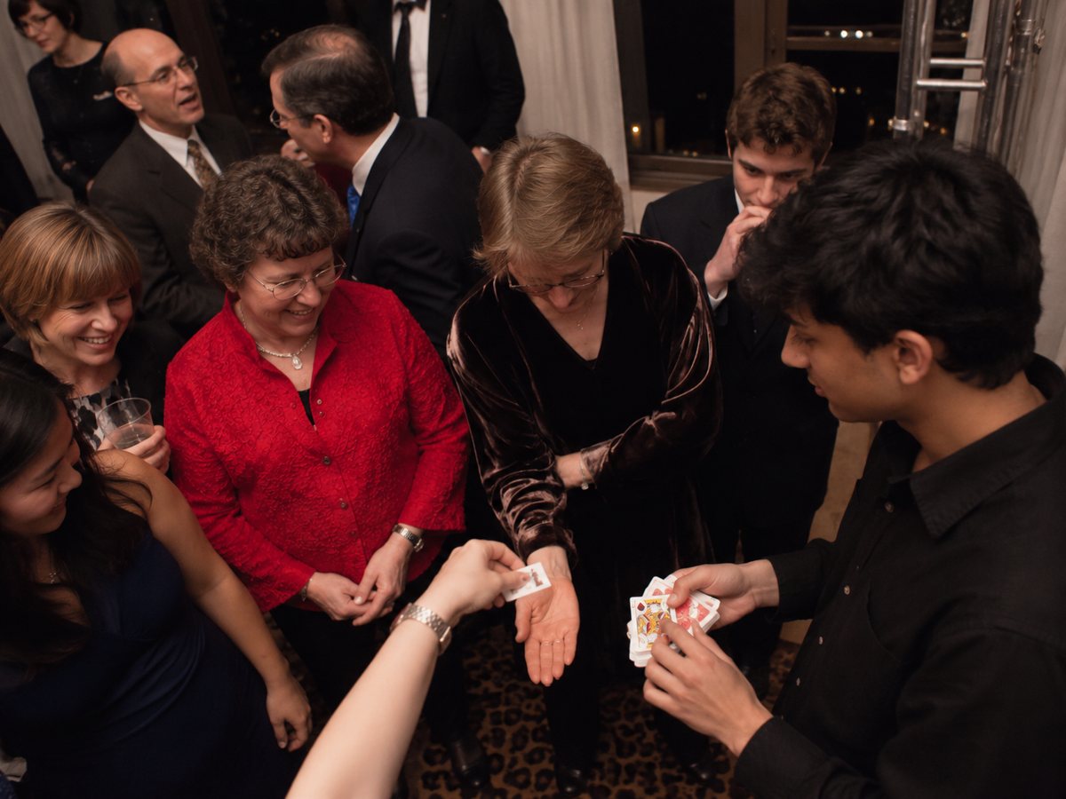 Guests gathered around Vihaan as a card appears in a guest's hand at a private dinner